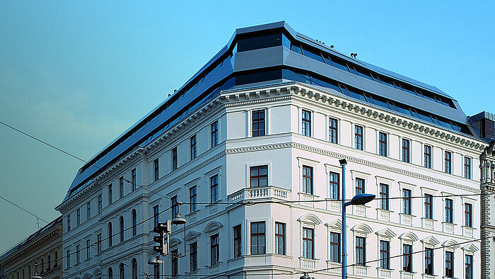 Corner of a white classical building with modern dark rooftop extension against blue sky