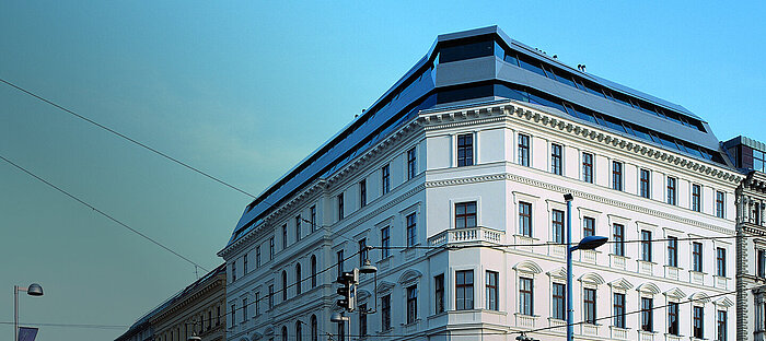 Corner of a white classical building with modern dark rooftop extension against blue sky