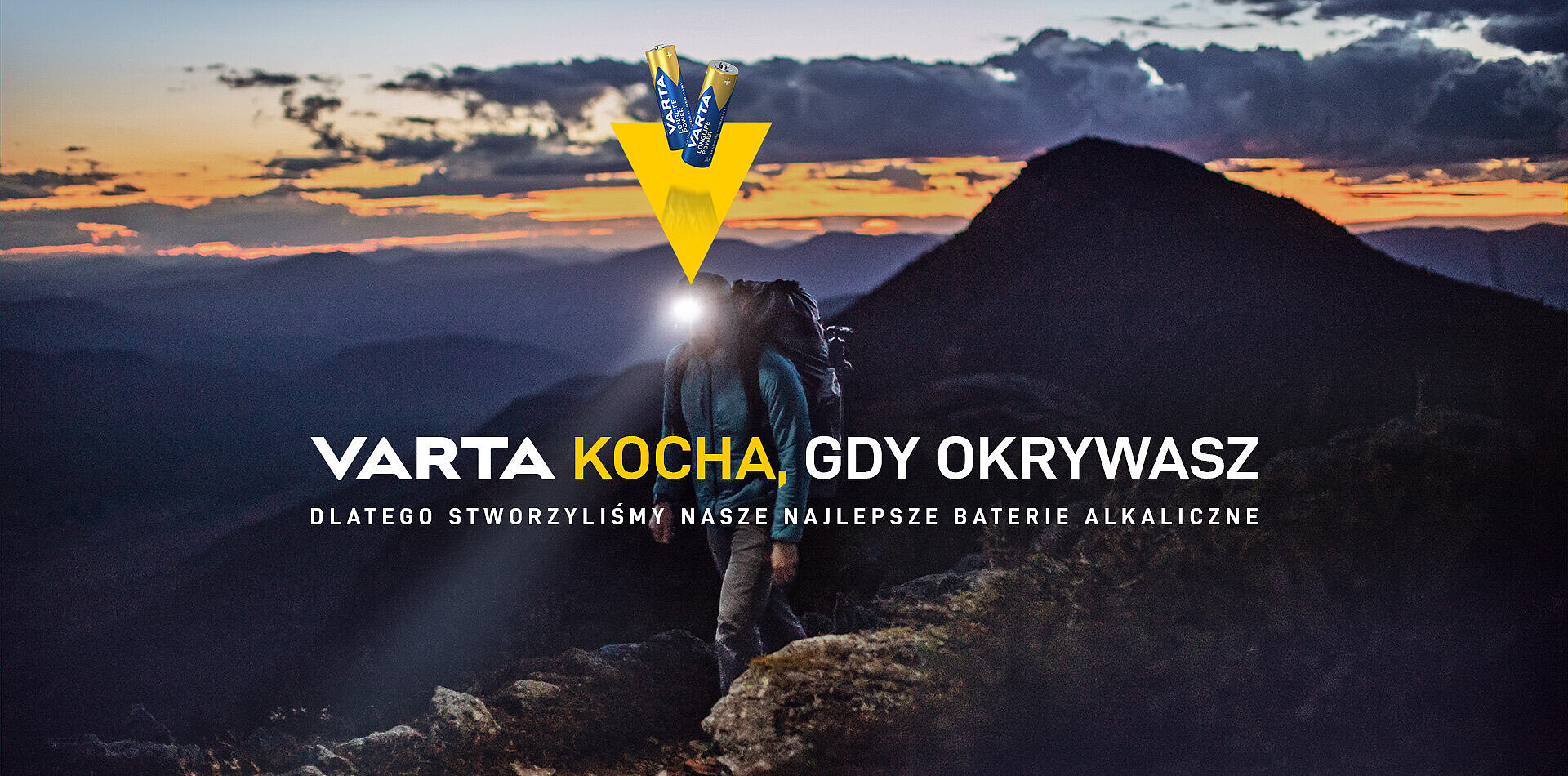 Wędrowiec z latarką czołową na górskim szczycie o zmierzchu, logo Varta z bateriami i hasło reklamowe