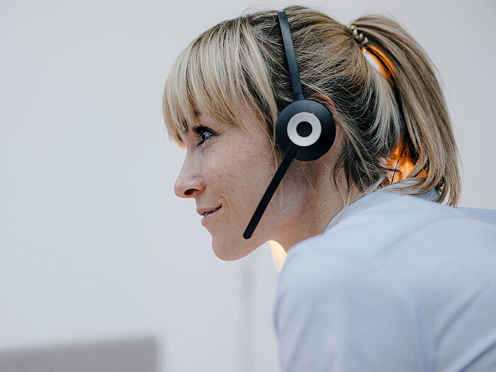 Seitenprofil einer blonden Frau mit Pferdeschwanz und Headset, die lächelnd nach vorne blickt