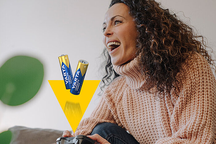 Femme souriante en pull beige tenant une manette de jeu, avec deux piles Varta et une flèche jaune en superposition
