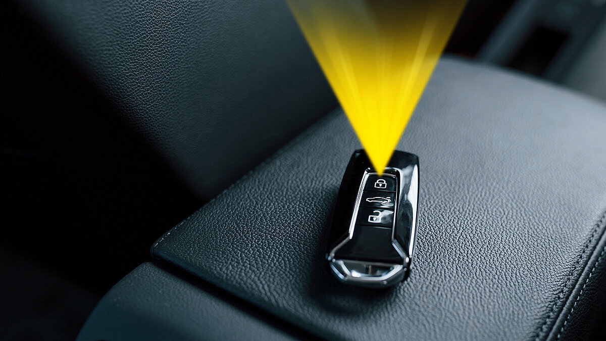 Modern car key fob on black leather seat emitting a yellow signal beam upward, symbolizing wireless transmission