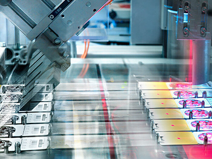 Automated production line with robotic arms assembling electronic components under red laser light in an industrial facility