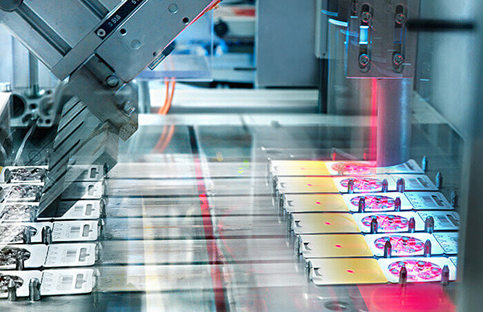 Automated production line with robotic arms assembling electronic components under red laser light in an industrial facility