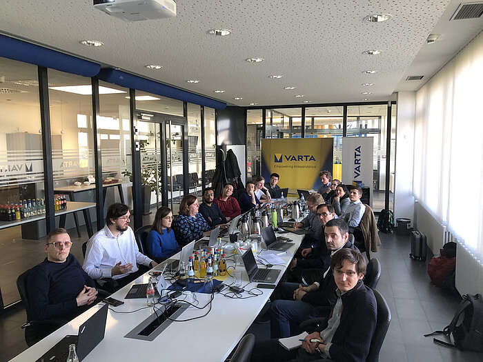 Gruppe von Personen sitzt an einem langen Konferenztisch mit Laptops, im Hintergrund ein VARTA-Banner