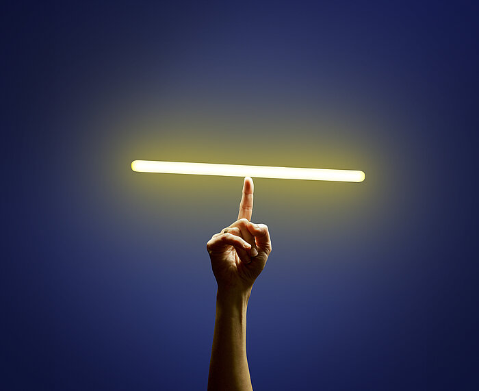 Hand with raised index finger balancing a glowing horizontal light tube against a dark blue background