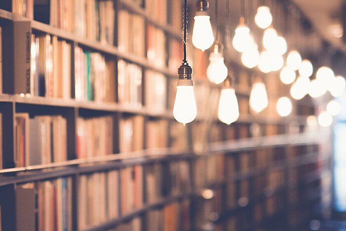 Bokhyller fylt med bøker i et bibliotek, opplyst av en rekke hengende lyspærer