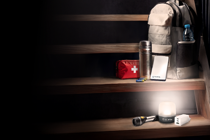 Emergency kit on stairs: backpack, water bottle, thermos, first aid bag, power bank, flashlight, LED lantern, USB charger