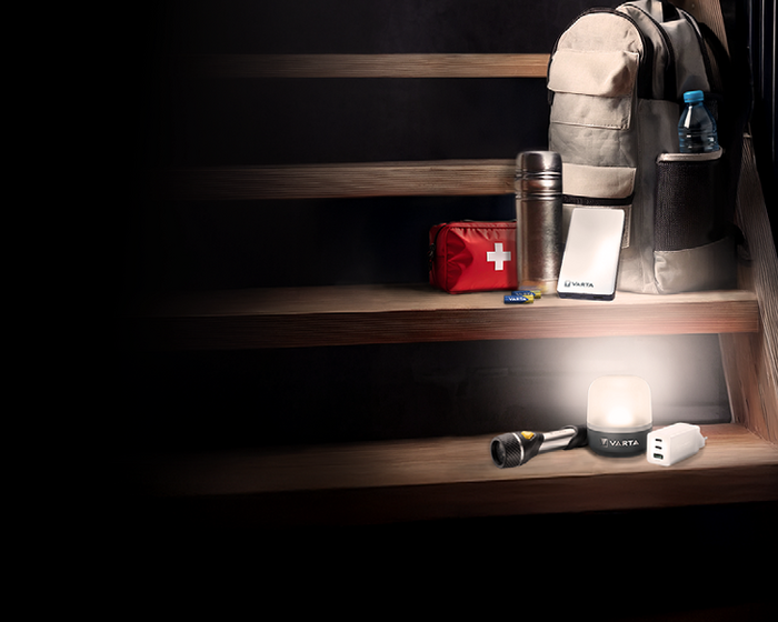 Emergency kit on stairs: backpack, water bottle, thermos, first aid bag, power bank, flashlight, LED lantern, USB charger