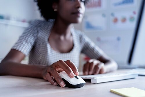 Close-up of a woman's hand using a computer mouse next to a keyboard at a desk