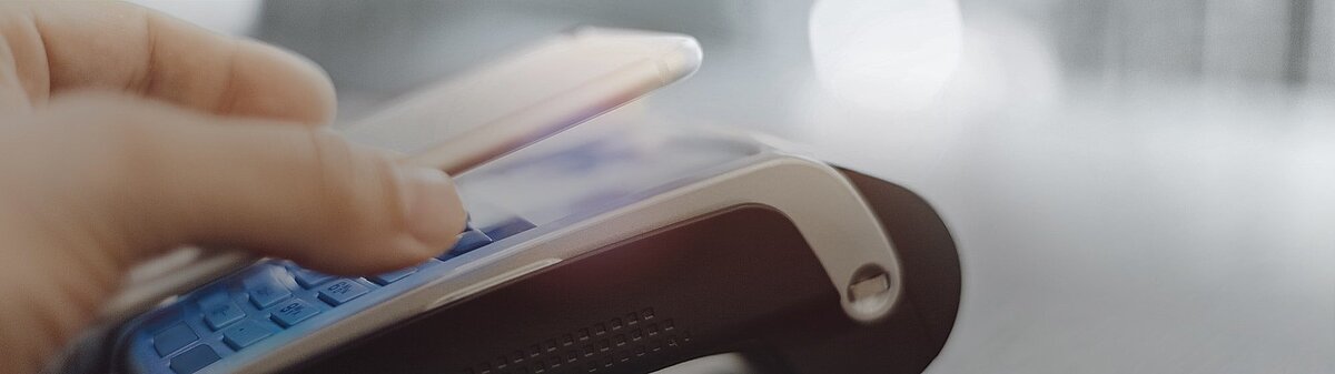 Close-up of a finger pressing buttons on a payment terminal keypad with a smartphone held above it