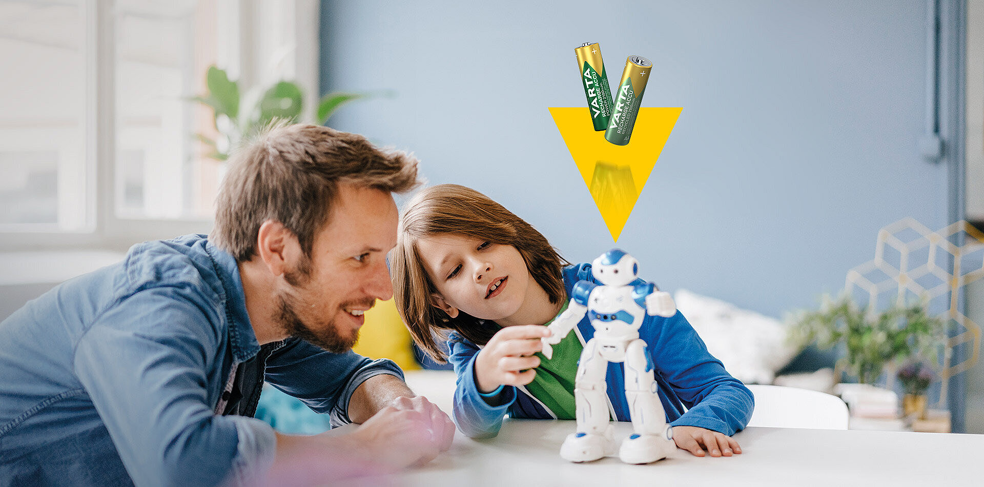 Ojciec i dziecko bawią się niebiesko-białym robotem, nad nimi dwie baterie Varta i żółty trójkąt