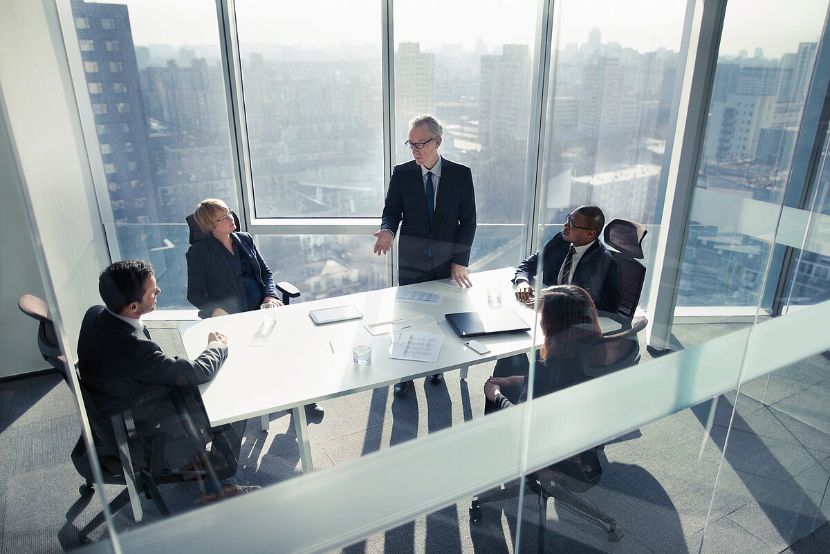 Five business professionals in a meeting around a conference table in a high-rise office with city skyline views