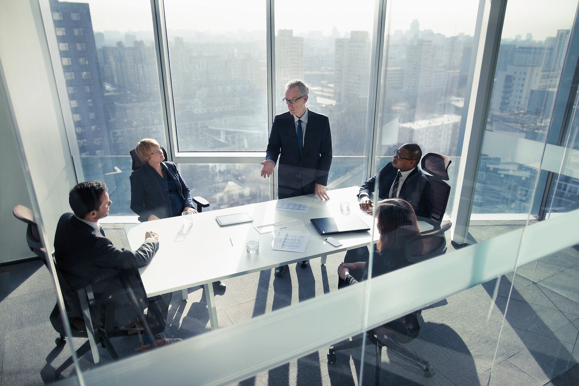 Five business professionals in a meeting around a conference table in a high-rise office with city skyline views