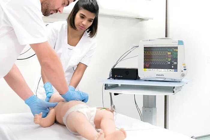 Zwei medizinische Fachkräfte untersuchen einen Säugling, daneben ein Philips-Monitor mit Vitalwerten