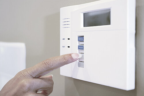 Finger pressing the police button on a wall-mounted white home security alarm keypad with medical and police buttons