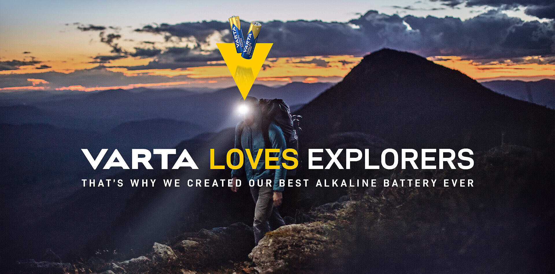 Horolezec s čelovkou na vrcholu hory za soumraku, nápis VARTA LOVES EXPLORERS a logo s bateriemi