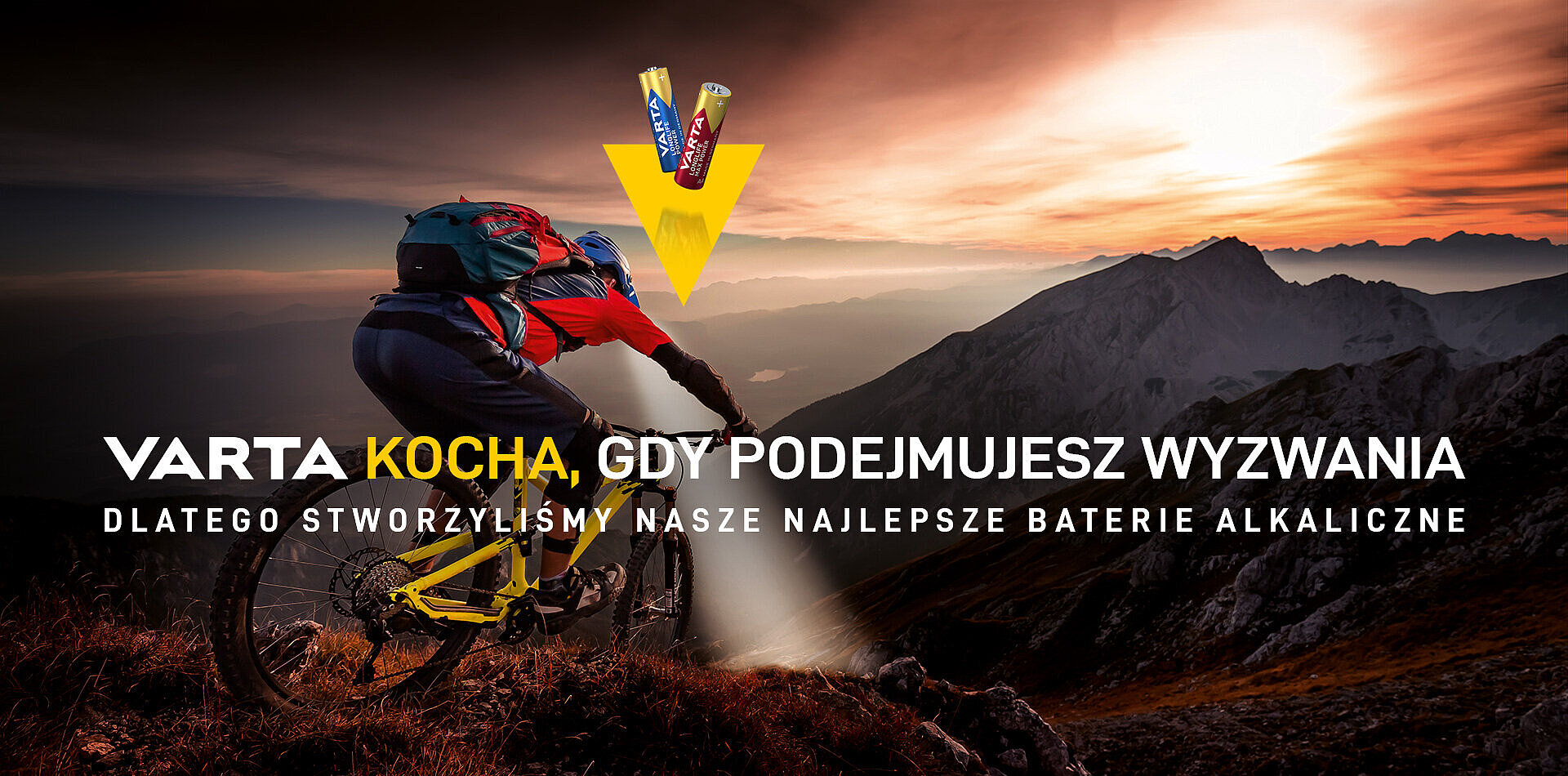 Rowerzysta górski na tle zachodu słońca w górach, powyżej dwie baterie Varta i hasło reklamowe o alkalicznych bateriach