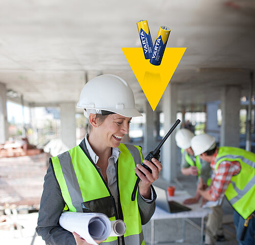 Smiling woman in hard hat and safety vest holds walkie-talkie; yellow arrow with Varta batteries points at her