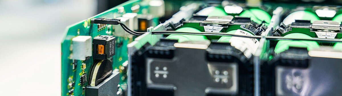 Close-up of green circuit board with black components, battery cells, wiring, and labeled chip reading HCI-R57 49CH13G