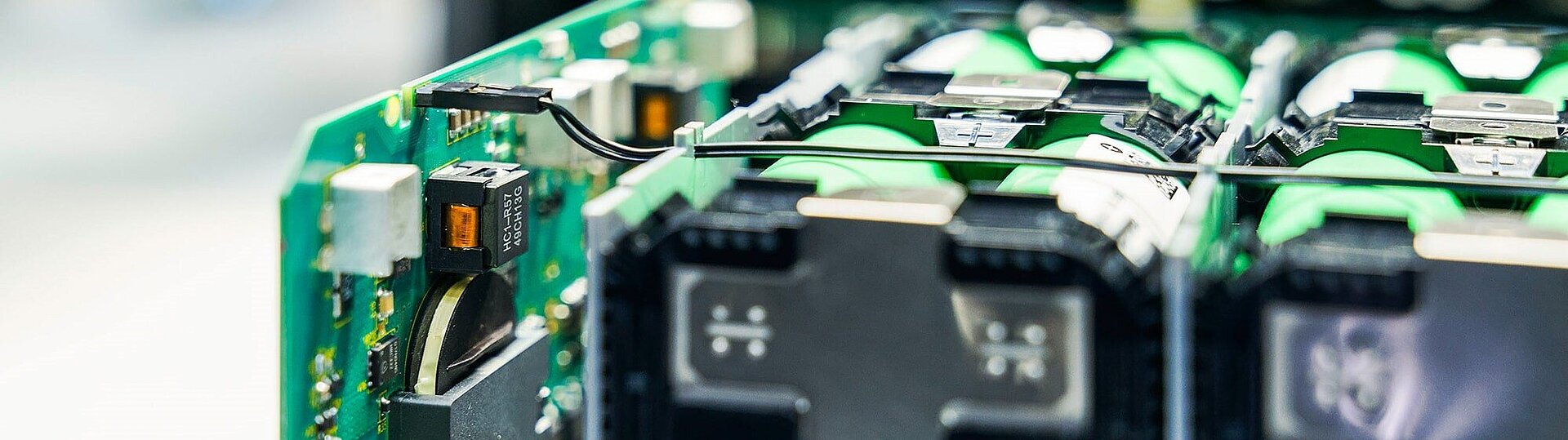 Close-up of green circuit board with black components, battery cells, wiring, and labeled chip reading HCI-R57 49CH13G