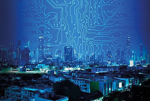 Nighttime city skyline in blue tones overlaid with circuit board patterns, symbolizing smart city technology
