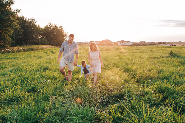 Familia con un niño caminando de la mano por un prado verde al atardecer, con casas al fondo
