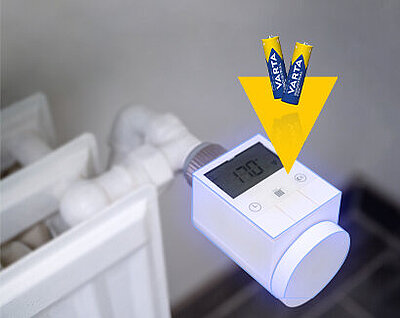 Smart radiator thermostat on heater showing 17°C, with two Varta batteries and yellow arrow indicating battery insertion