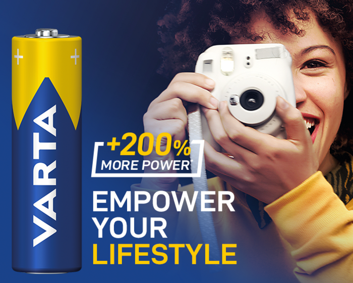Varta-Batterie neben lachender Frau mit Sofortbildkamera, Text: +200% More Power, Empower Your Lifestyle