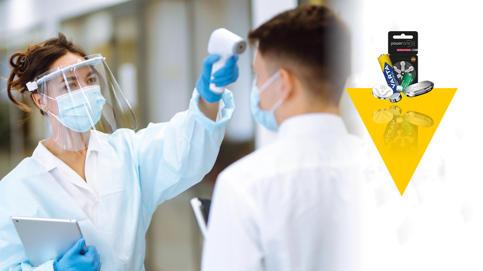 Healthcare worker in face shield and mask uses infrared thermometer on patient; batteries shown in yellow triangle