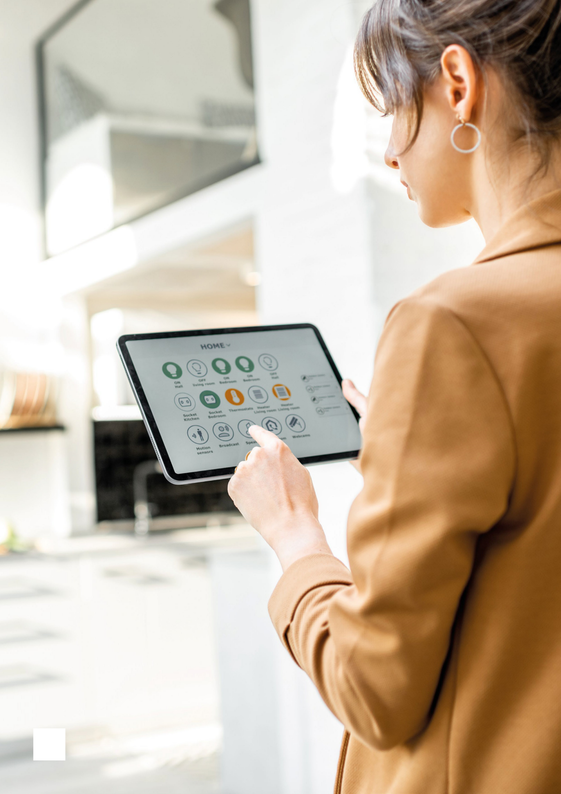 Woman in beige top holding a tablet displaying a smart home control app with icons for lights, sockets, and sensors