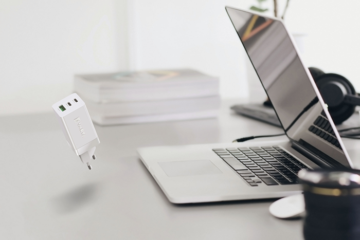 Weißes USB-Ladegerät schwebt über Schreibtisch neben aufgeklapptem Laptop, Kopfhörern, Büchern und Kamera