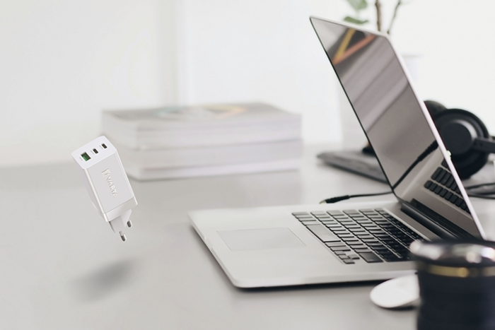 Chargeur USB blanc en lévitation au-dessus d'un bureau avec ordinateur portable, casque, livres et appareil photo