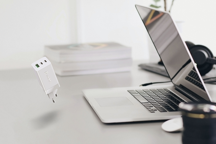 Vit USB-laddare svävar över skrivbord med bärbar dator, böcker, hörlurar och kameraobjektiv
