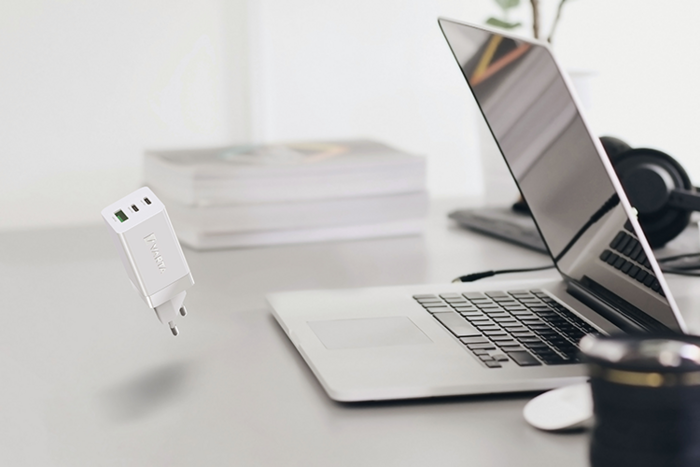 Hvit USB-lader svever over skrivebord med åpen bærbar PC, hodetelefoner, bøker og kameralinse i bakgrunnen