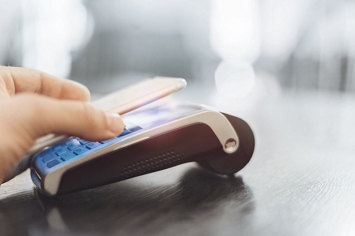 Hand holding a smartphone over a card payment terminal on a dark surface for contactless payment