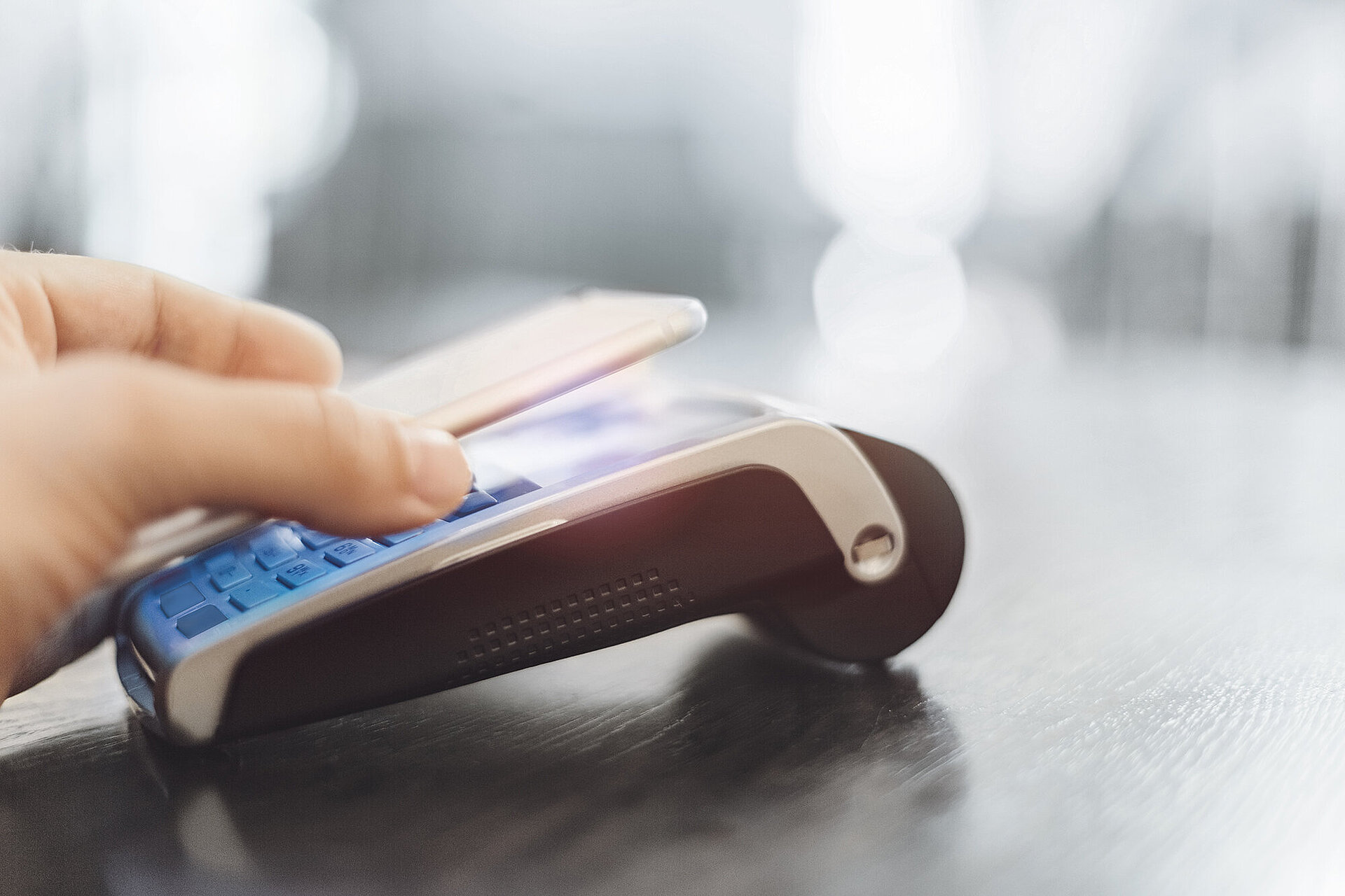 Hand holding a smartphone over a card payment terminal on a dark surface for contactless payment