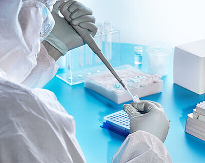 Scientist in protective suit and gloves uses a multichannel pipette on a microplate in a laboratory