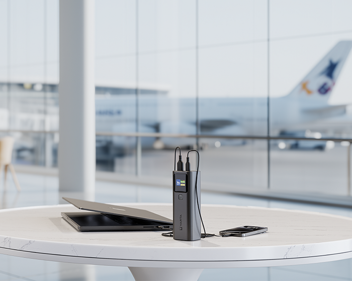 Power bank charging a laptop and smartphone on a round table in an airport lounge with an airplane visible outside