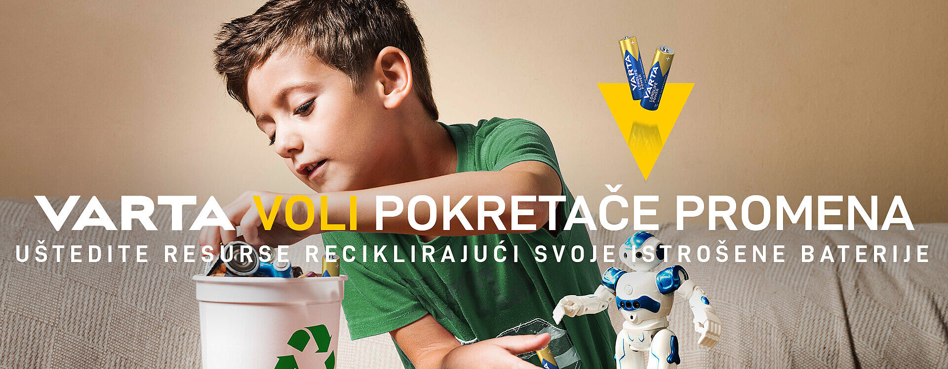 Dečak u zelenoj majici ubacuje baterije u kantu za reciklažu pored robota igračke, natpis VARTA voli pokretače promena