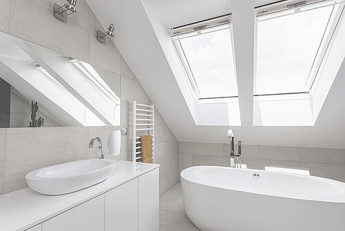 Modern attic bathroom with two skylights, white vessel sink on vanity, freestanding tub and heated towel rail