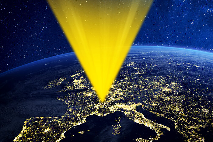 Yellow beam of light descending from space onto illuminated Europe seen at night from orbit with stars in background