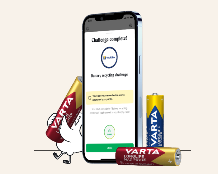 Smartphone zeigt abgeschlossene Batterie-Recycling-Challenge der Varta-App, daneben Comic-Huhn und drei Varta-Batterien