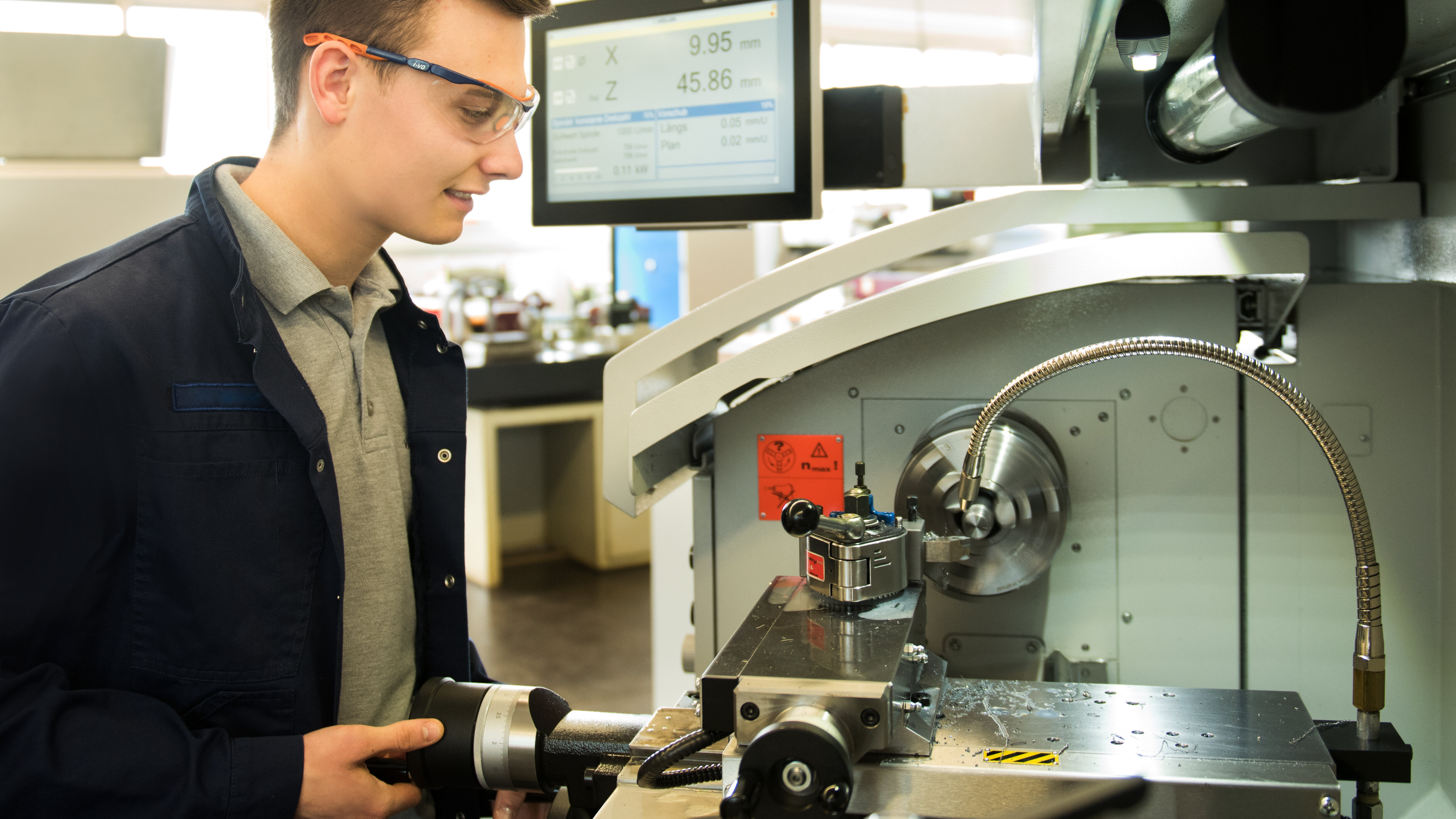Junger Mann mit Schutzbrille bedient eine Werkzeugmaschine mit digitalem Display, das Messwerte anzeigt