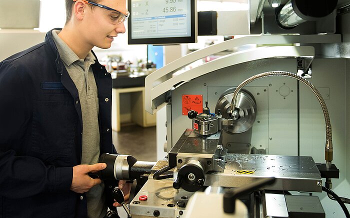 Junger Mann mit Schutzbrille bedient eine Werkzeugmaschine mit digitalem Display, das Messwerte anzeigt