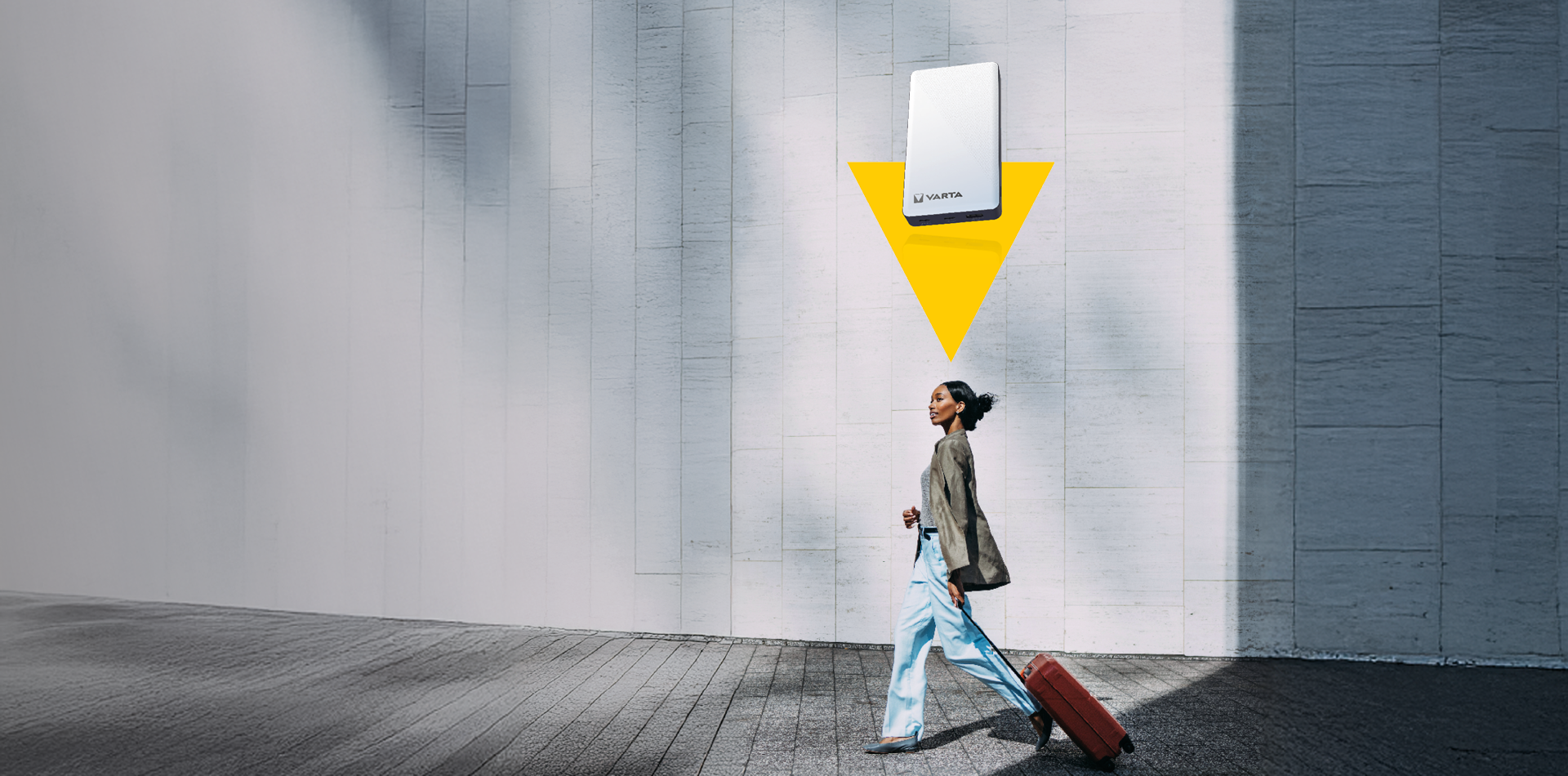 Femme tirant une valise rouge devant un mur clair, batterie externe Varta blanche et flèche jaune au-dessus d'elle